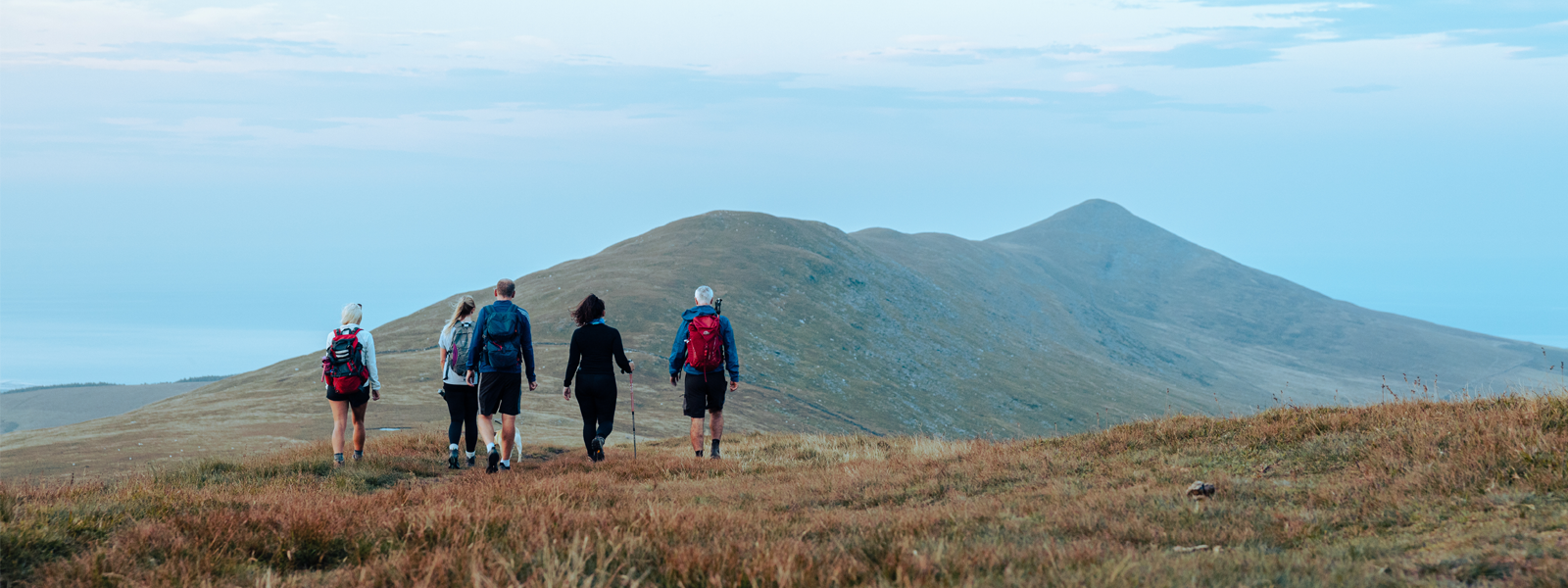 A group of walkers descending down a summit on the Isle of Man with their backs to the camera 